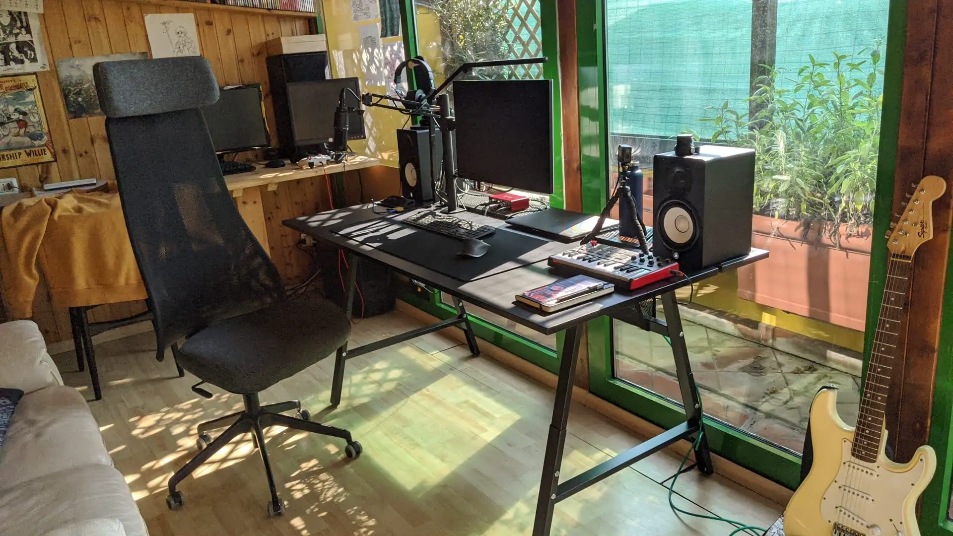 Desk beside a window with a monitor, laptop and guitar
