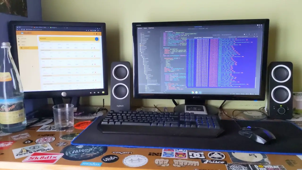 Two monitors and speakers on a desk covered in stickers
