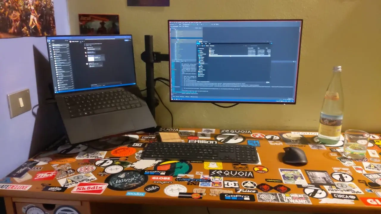 Laptop and external display on a desk covered in stickers